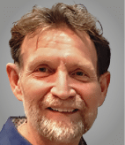 A man with a beard and mustache smiling. Description generated by AI