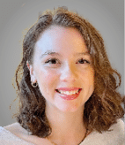 A person with shoulder-length wavy hair is smiling warmly against a plain gray background. Description generated by AI