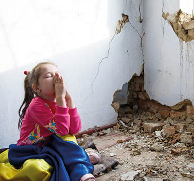 A Ukrainian child prays for an end to the war. Consequences of the Russian war against Ukraine. War in Ukraine. Children against war. Peace concept. A child in front of a war-torn house.
