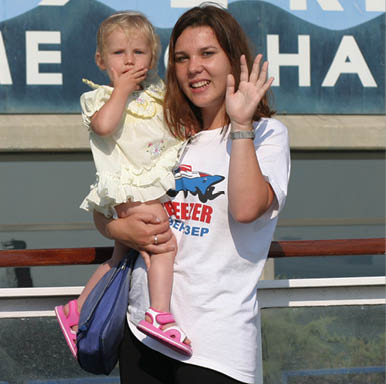A woman holding a child in front of a sign that says Welcome to Haifa. Description generated by AI