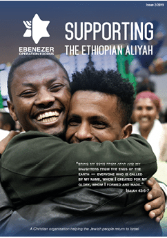 Two adults embrace warmly in a crowded indoor setting with text promoting support for Ethiopian Aliyah and a biblical quote from Isaiah 43:6-7. Description generated by AI
