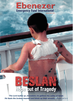 A child with a bandaged back and visible bruises sits on a white chair on a boat with a cloudy sky and water in the background, accompanied by text about hope and tragedy related to Beslan. Description generated by AI