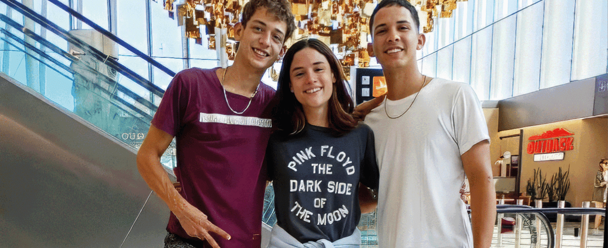 Three people standing in front of a large chandelier. Description generated by AI