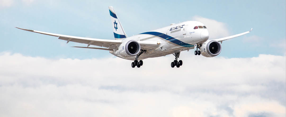A large white airplane with a blue and white tail flying in the sky. Description generated by AI