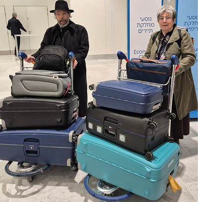 A man and woman standing next to a cart full of luggage. Description generated by AI