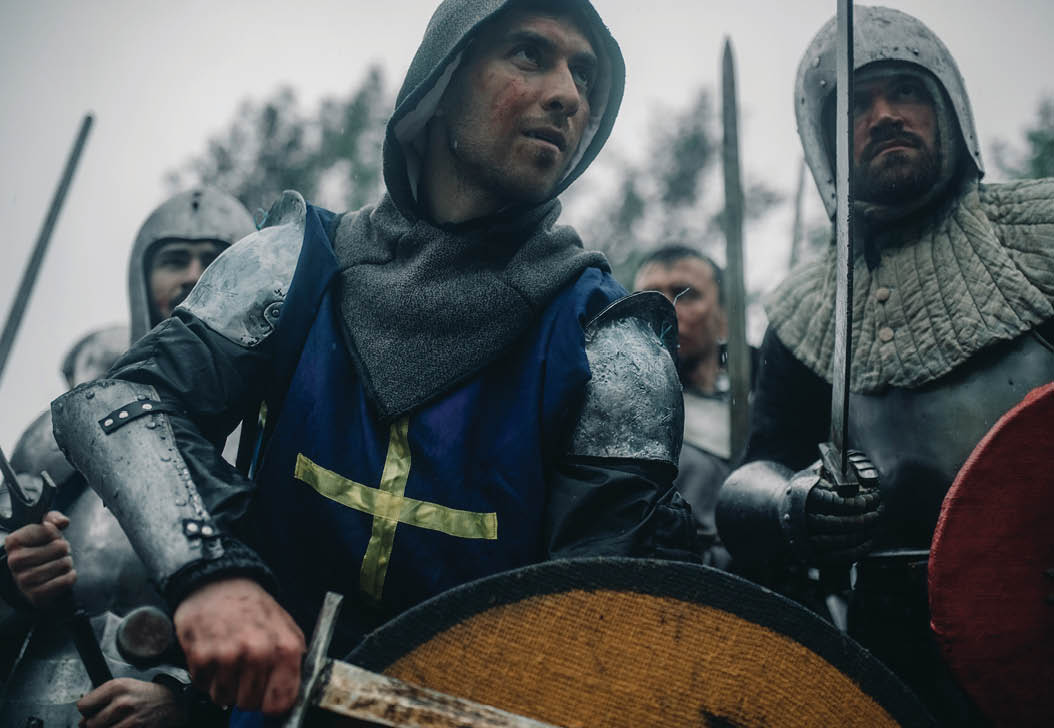 Combat squad of medieval knights of the Crusaders stand in armors and helmets with their swords and shields preparing to attack.