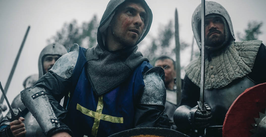 Combat squad of medieval knights of the Crusaders stand in armors and helmets with their swords and shields preparing to attack 