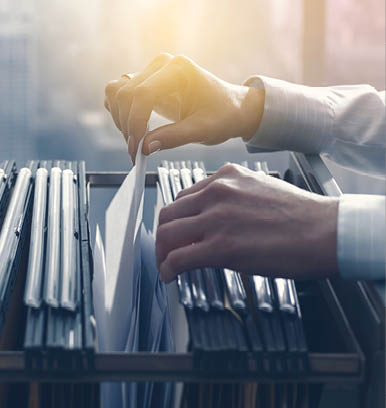 Professional female office clerk searching files and paperwork in the filing cabinet