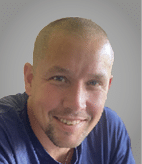 A person with short hair wearing a blue shirt is sitting against a plain gray background. Description generated by AI