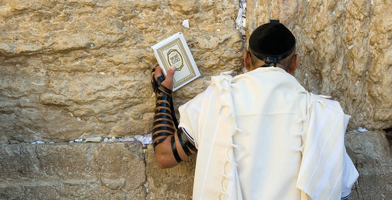 JERUSALEM, ISRAEL - OCT 06, 2014: A jewish man with the torah in his hand is praying against the western wall in the old city of Jerusalem